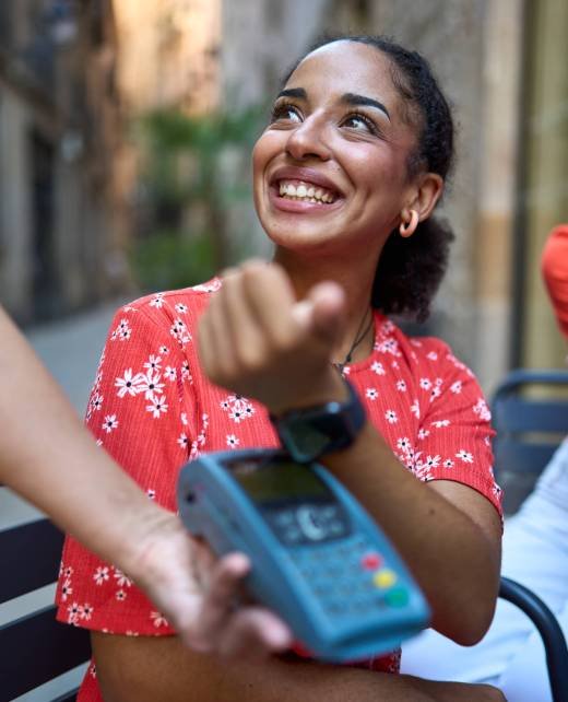 Vertical close-up portrait of a latin woman using smart watch to pay in an outdoors cafeteria